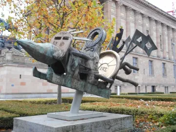 Humpty Dumpty sculpture with bronze mechanical forms, a golden disc marked \