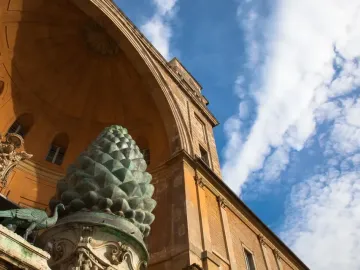 La Pigna bronze pine cone sculpture with a peacock beside it in a courtyard