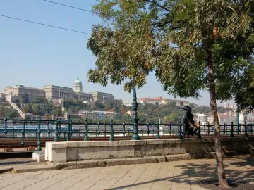 Little Princess statue sitting on a railing with a river and cityscape in the background.