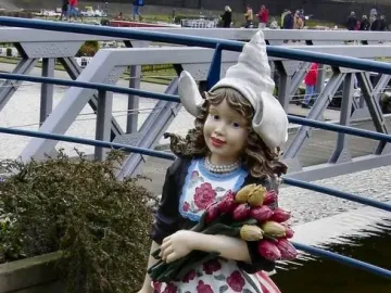 Madurodam statue of a Dutch girl in traditional dress holding tulips and wearing clogs beside the water.