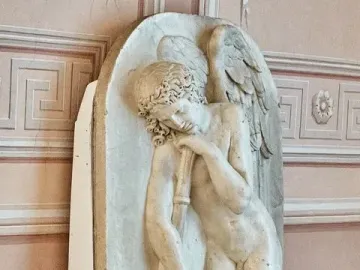 Marble bas-relief of a winged nude male figure leaning on a staff with a floral wreath, set against a pink decorative wall.