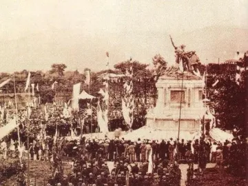 The National Monument of Costa Rica stands on a tiered base, surrounded by a large crowd and flags during a public ceremony.