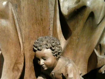 Wooden sculpture of Saint Luke as a curly-haired child kneeling with one hand extended.