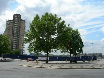 Traffic Light Tree sculpture made from dozens of traffic lights, with some lights glowing red and amber, on a roundabout island near a tall building.