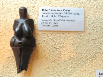 Venus of Dolní Věstonice figurine with prominent breasts and a rounded belly, displayed beside a multilingual label.