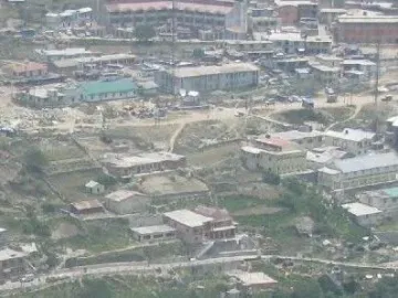Aerial view of a town spread across a valley beside a winding river, framed by rocky foreground outcrops.