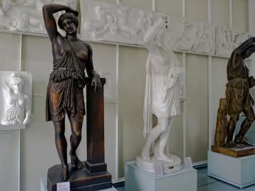 Classical Amazon statues displayed in a museum gallery, with three draped female figures standing before relief panels.