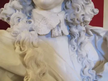 Close-up of the Bust of Francesco I d\'Este showing the marble curls, cravat, and draped clothing against a red background.