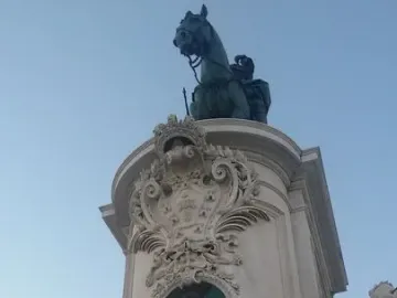 Equestrian Statue of Joseph I on a tall ornate pedestal with marble figures and reliefs against a blue sky.