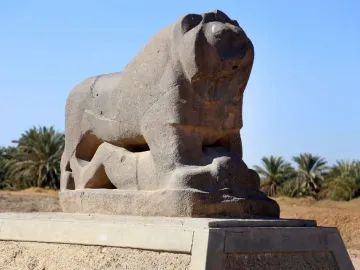 The Lion of Babylon stone sculpture resting on a base beneath a clear blue sky.