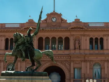 Manuel Belgrano equestrian monument in front of a pink building with arched windows and a central clock.