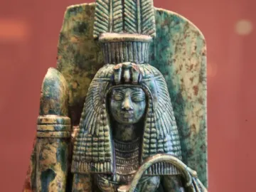 Weathered bust of Queen Tiye with an ornate headdress and heavy wig, shown in close-up.