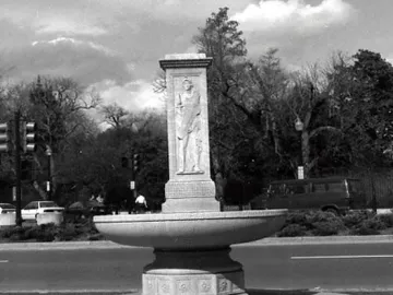 Butt–Millet Memorial Fountain standing in a grassy median with a tall rectangular stone shaft and circular basin