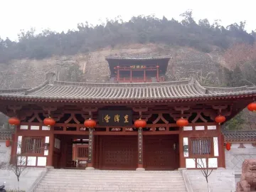 Huangze Monastery entrance with red columns, hanging lanterns, and a stone staircase against a rocky mountainside.