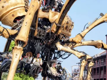 La Princesse, a giant mechanical spider, with people seated in platforms beneath its body against a blue sky.