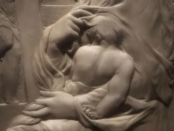 Madonna of the Stair marble relief showing a child nestled against an adult figure with hands supporting the child.