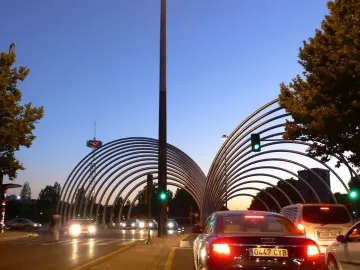 Puerta de la Ilustración arches over a road in Madrid at twilight, with cars passing underneath.