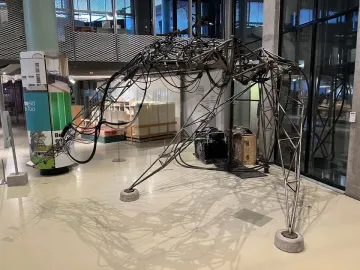 The Senster sculpture with an arched skeletal metal frame, three legs, and cables draped across its structure.
