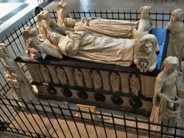 The Tomb of Francis II of Brittany with two recumbent crowned effigies, surrounded by carved figures and enclosed by a black metal fence.