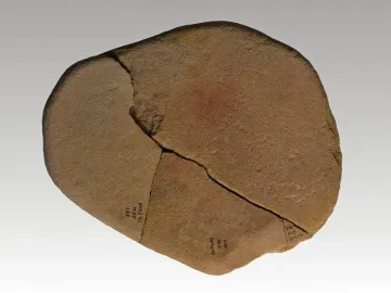 Reddish-brown stone fragment from the Venus of Monruz, with a prominent crack and faint black markings.