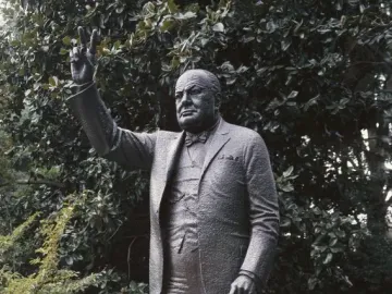 Winston Churchill statue holding a cane and raising a V sign outdoors.