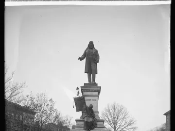 Albert Pike Memorial showing a bearded man in a long coat atop an ornate stone pedestal with a seated figure below and bare trees around it.