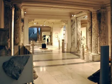 The Athlete from Ephesus standing on a pedestal in a columned museum hall, seen from behind.