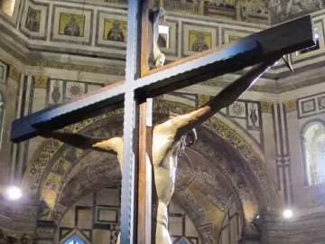 Brunelleschi Crucifix displayed in a decorated church interior with visitors gathered below.