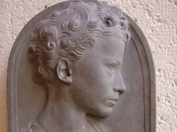 Bust of a Child in gray stone, shown in profile with curly hair and draped shoulders.