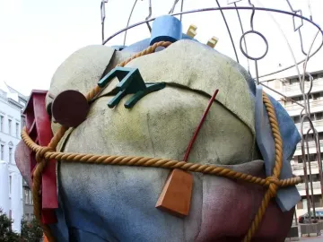 Houseball sculpture with a large textured sphere in yellow, blue, and red, wrapped with a rope and attached abstract forms.