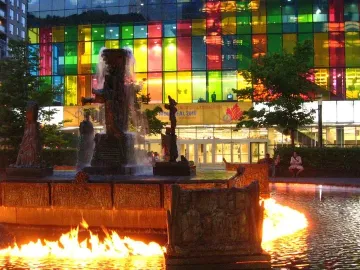 La Joute bronze fountain with water cascading from the center and flames burning on the surrounding pool.