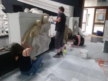 Workers restoring large Parthenon metopes in a studio filled with plaster casts.