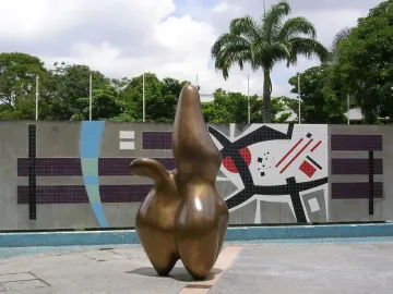 Cloud Shepherd, a bronze abstract sculpture with rounded forms and a central peak, stands in front of a geometric tiled wall.