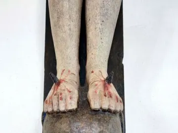 Close-up of the Enghausen Cross showing the nailed feet of the crucified figure resting on a carved head with blue eyes.
