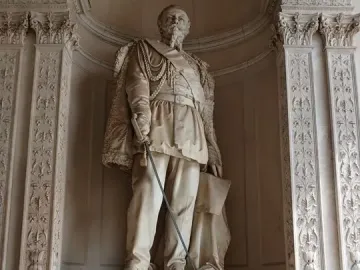 Monument to Vittorio Emanuele II showing a marble statue of a man in military uniform holding a sword and a document above an inscribed pedestal.