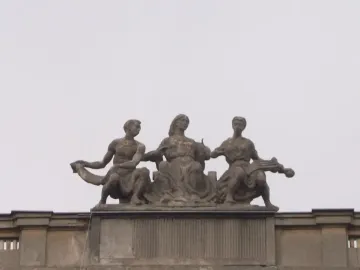 Music sculpture with three seated figures on a rooftop in Warsaw, including a central woman with outstretched hands and a woman holding a stringed instrument.