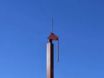 The Pink Panther sculpture rises from a shallow reflecting pool beneath a clear blue sky.