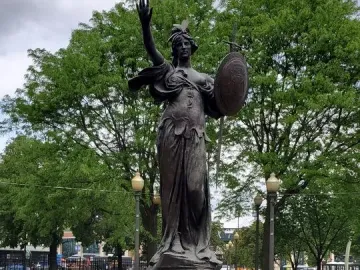Russell Alger Memorial Fountain with a bronze draped female figure holding up an arm and shield atop a stone pedestal.