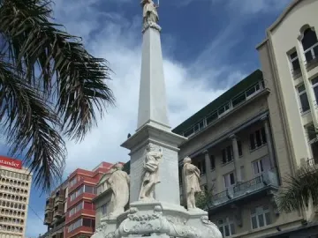 The Triumph of the Candelaria monument, a white stone obelisk with carved figures at the base and a statue on top, in a city square