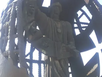 Detail of the Birth of a New Man sculpture showing a dark figure holding a scroll, framed by a rope lattice and ship mast.