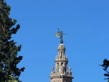 The Giraldillo statue atop a tall tower, with a circular shield against a clear blue sky.