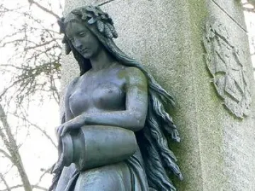 Mutter Kinzig statue of a bronze-colored woman holding an urn beside a stone monument
