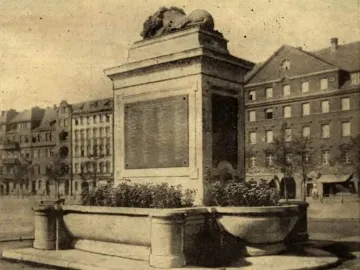 Sleeping Lion sculpture resting atop a stone monument with its head lowered and turned slightly.