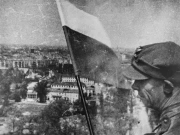 A soldier stands beside a two-toned flag with the Victory Column overlooking Berlin.