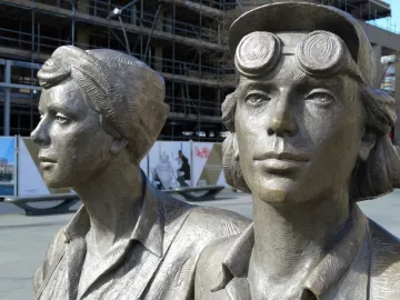 Close-up of two figures from the Women of Steel sculpture, one wearing a cap with goggles on the brim.