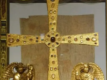 The Cross of the Angels, a jeweled golden cross displayed in a glass case with kneeling angel figures beside it.