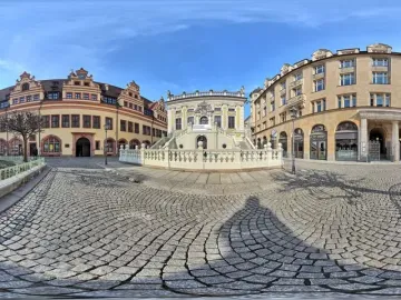 Goethe Monument on a reddish-brown pedestal beside a cobbled square in Leipzig.
