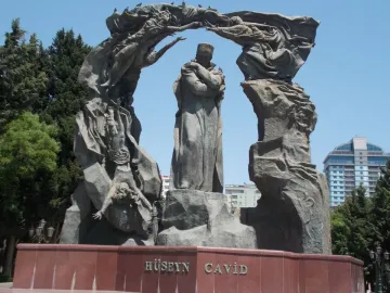 Huseyn Javid monument with a central robed figure, flanked by tall sculptural forms and arching figures above a red stone base.