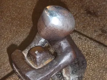 Järnpojke, a small dark metal seated figure hugging its knees, with coins scattered around the base.