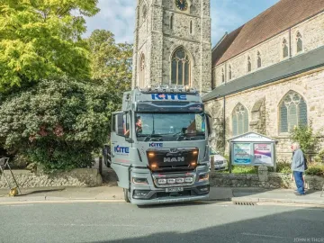 A large KITE Haulage Ltd truck parked on a street beside a stone church with a tall clock tower.